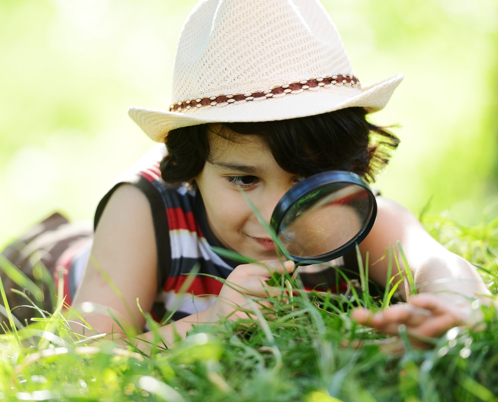 Curious gifted child in a hat is exploring nature by looking intently through a magnifying glass.